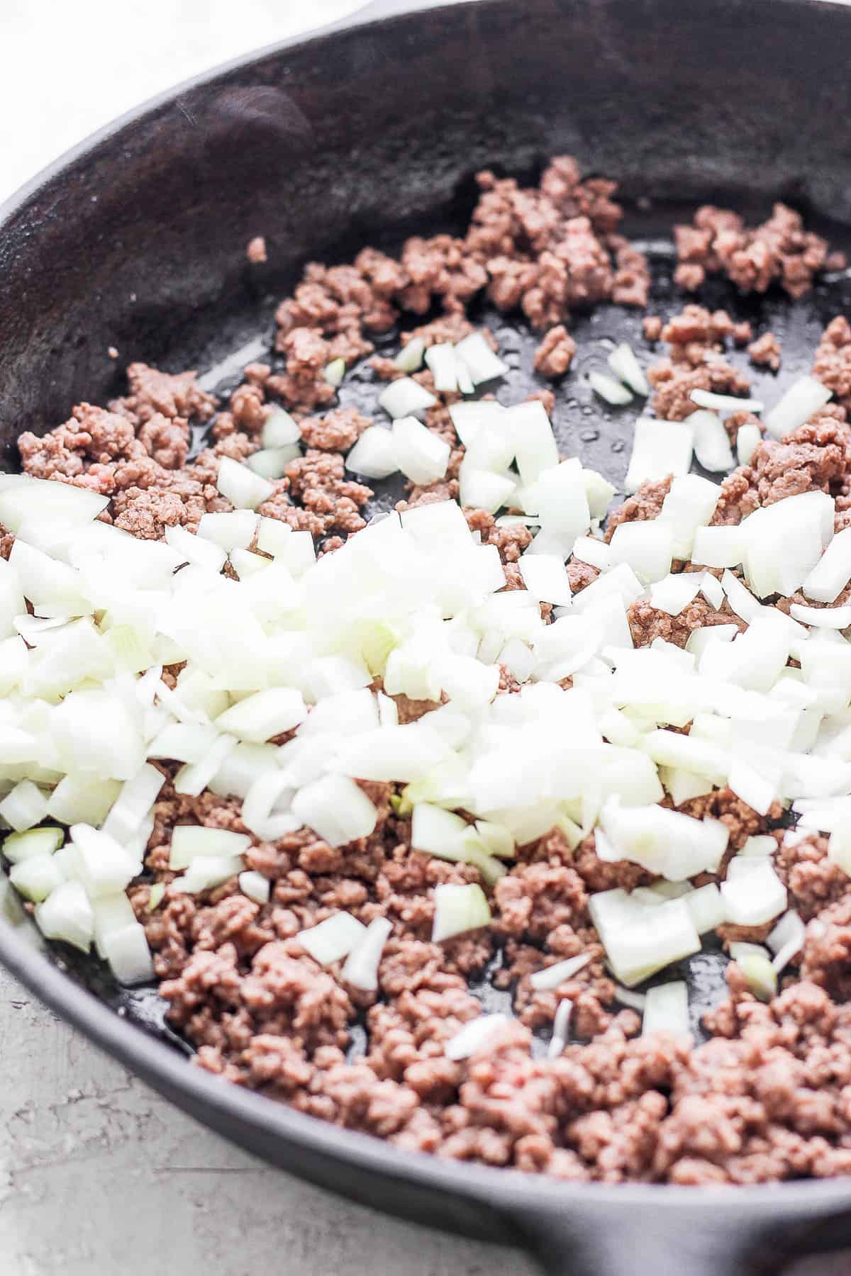 Side view of a cast iron skillet with cooked ground beef and onion. 