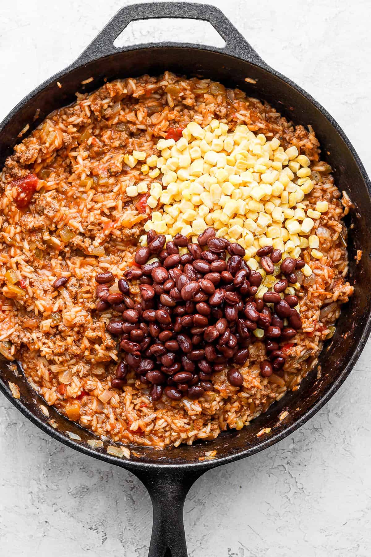 Cast iron skillet with mexican rice inside along with corn and black beans.