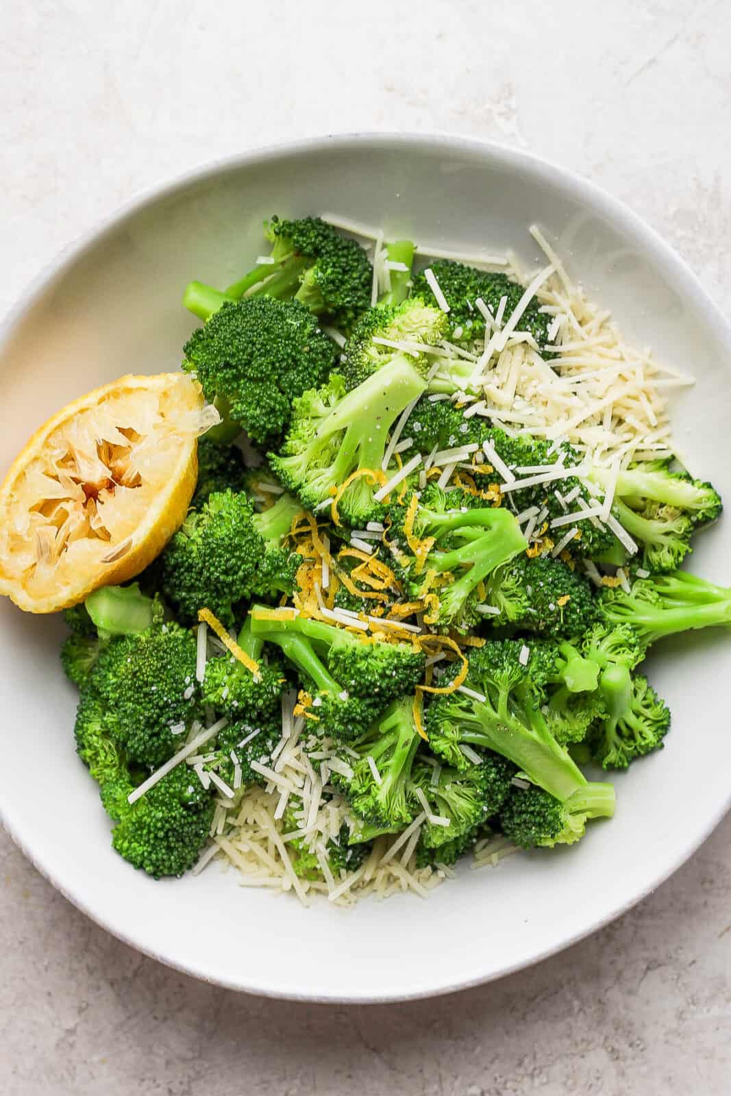 Bowl of parmesan broccoli with a lemon wedge.