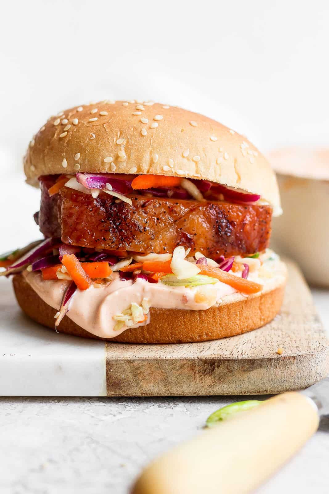 A crispy pork belly sandwich on a cutting board.