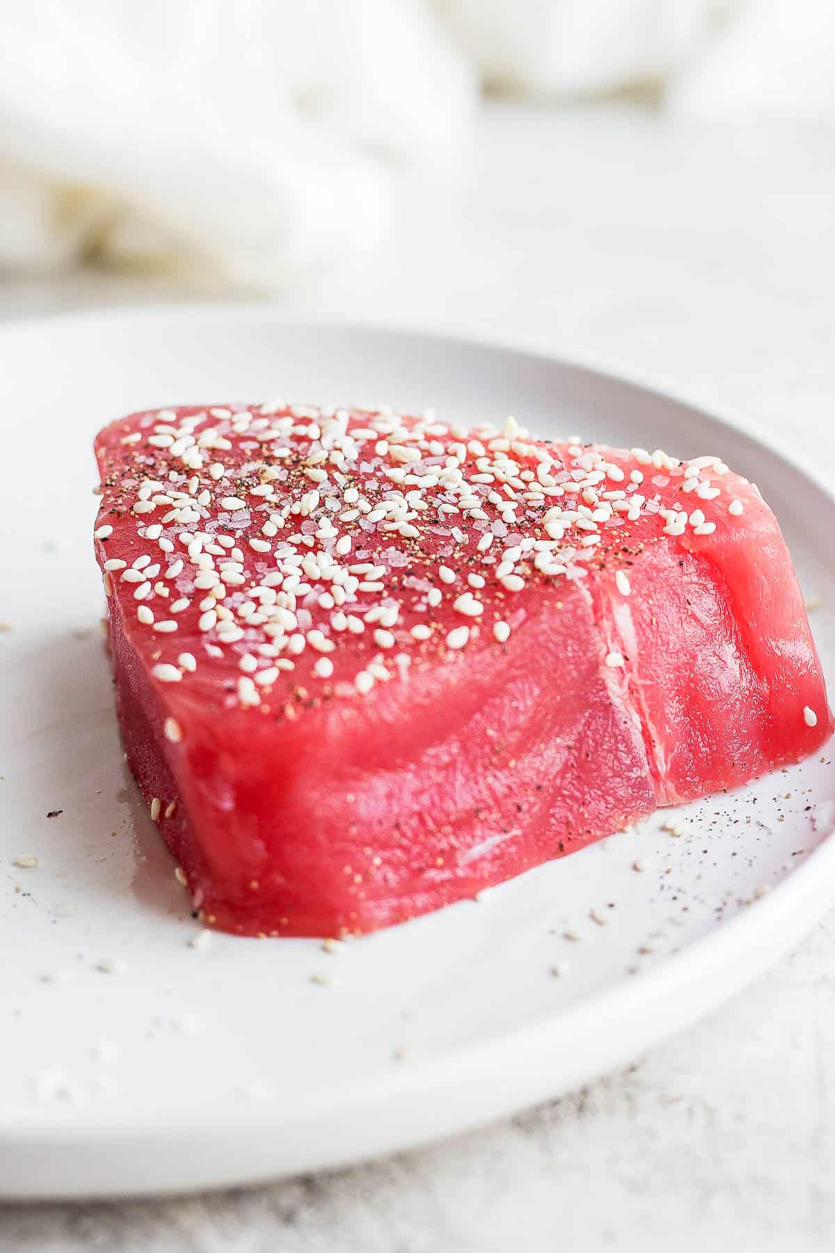 A tuna steak on a plate seasoned with salt, pepper, and sesame seeds.