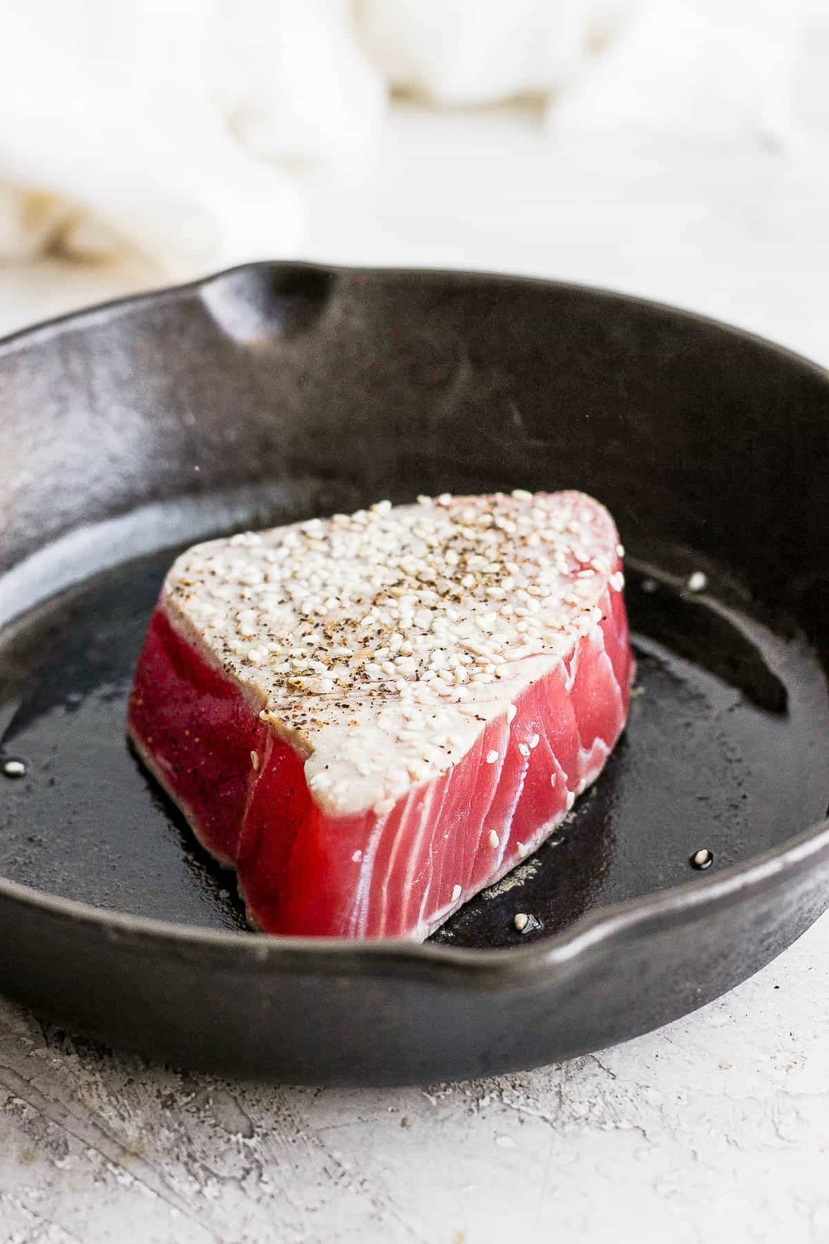 A seasoned tuna steak searing in a large cast iron skillet.