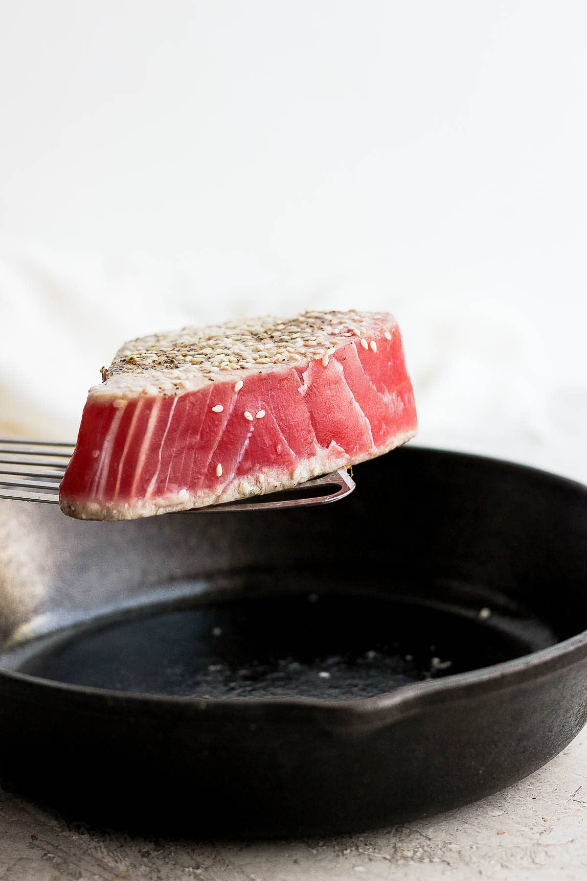 Someone lifting a piece of seared ahi tuna out of cast iron skillet. 