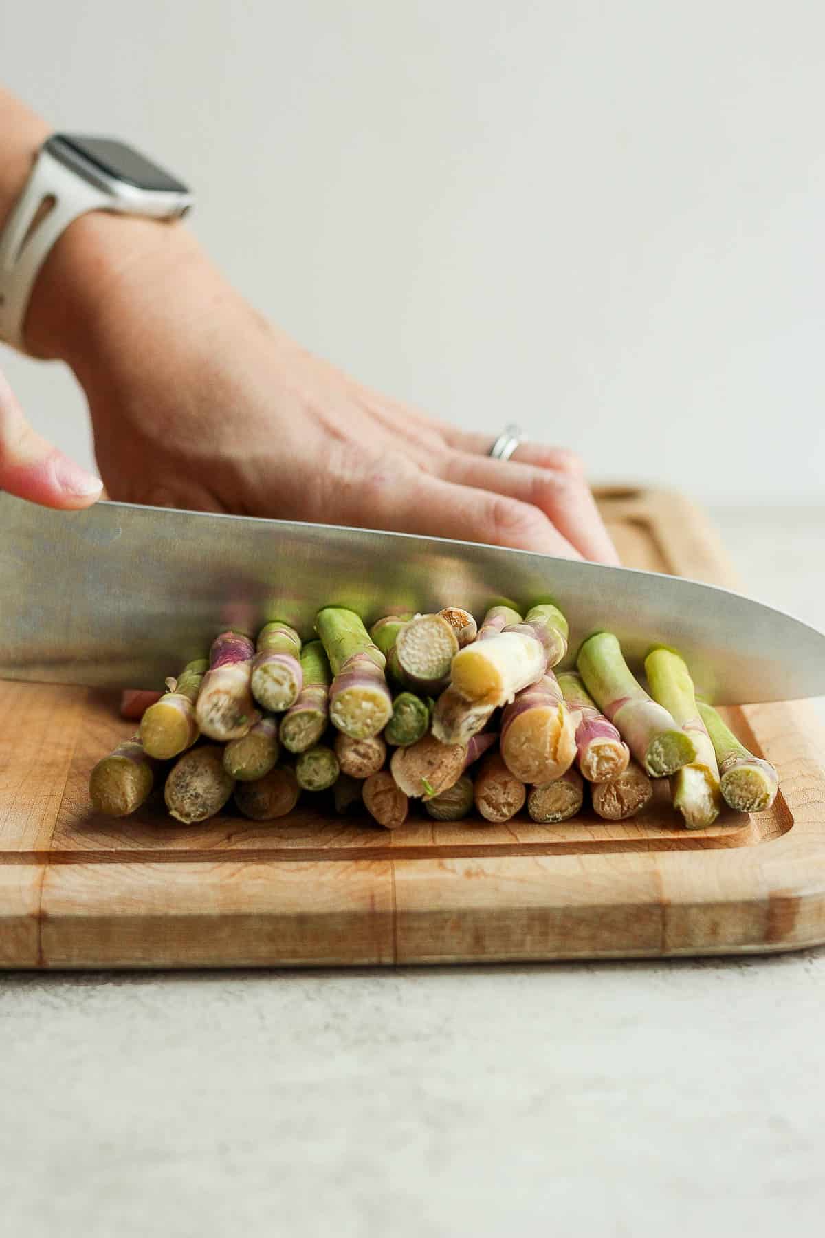 A large knife cutting the thick ends off the asparagus stalks on a cutting board.
