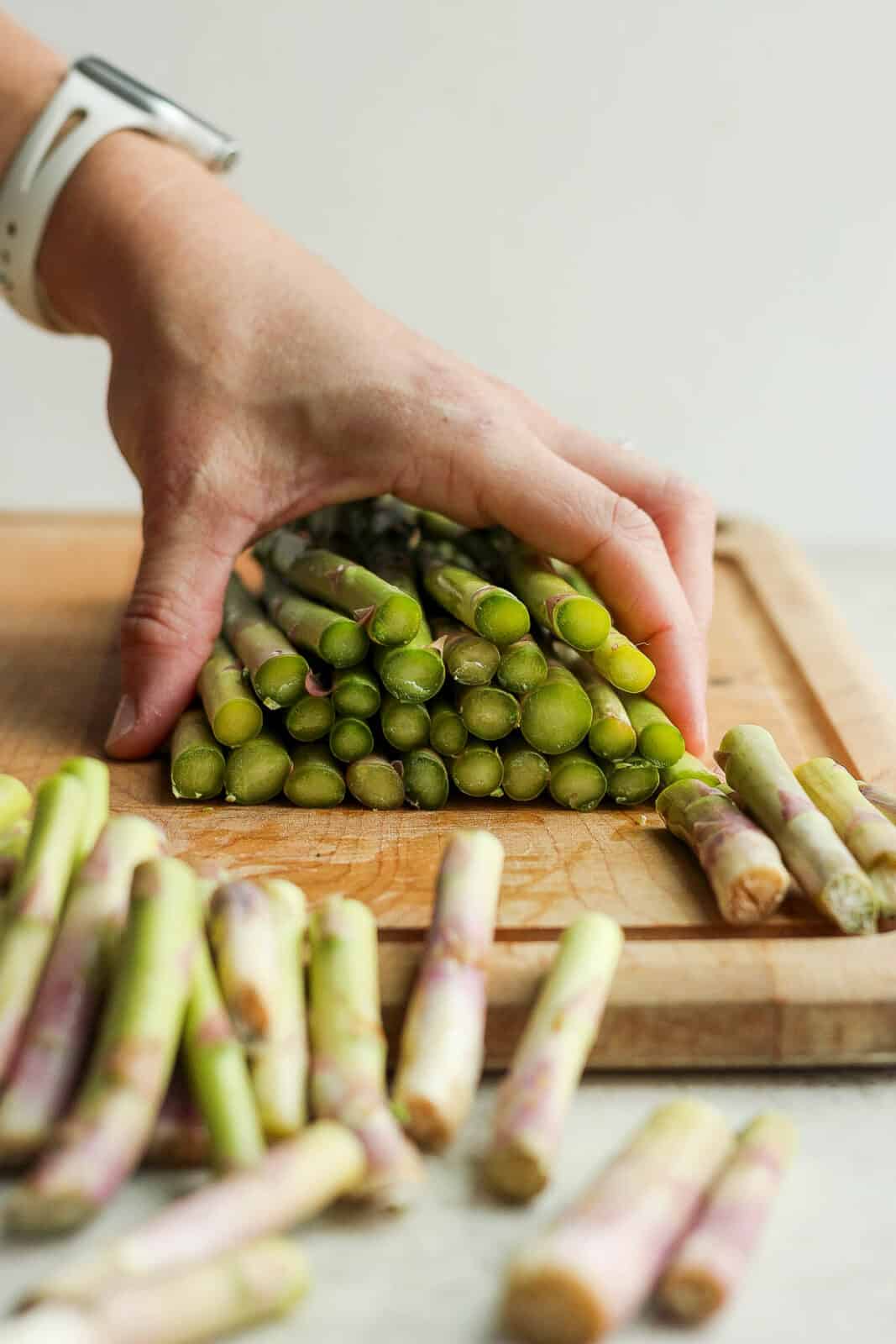 A bunch of asparagus with their ends cut off on a wood cutting board.