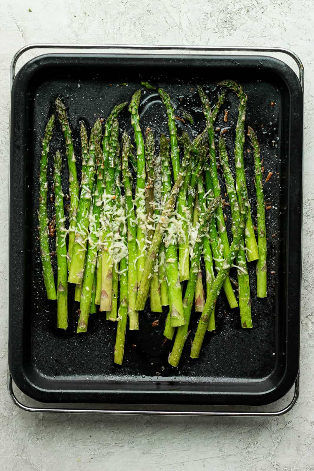Air fryer asparagus on a black baking sheet with salt and melted parmesan.