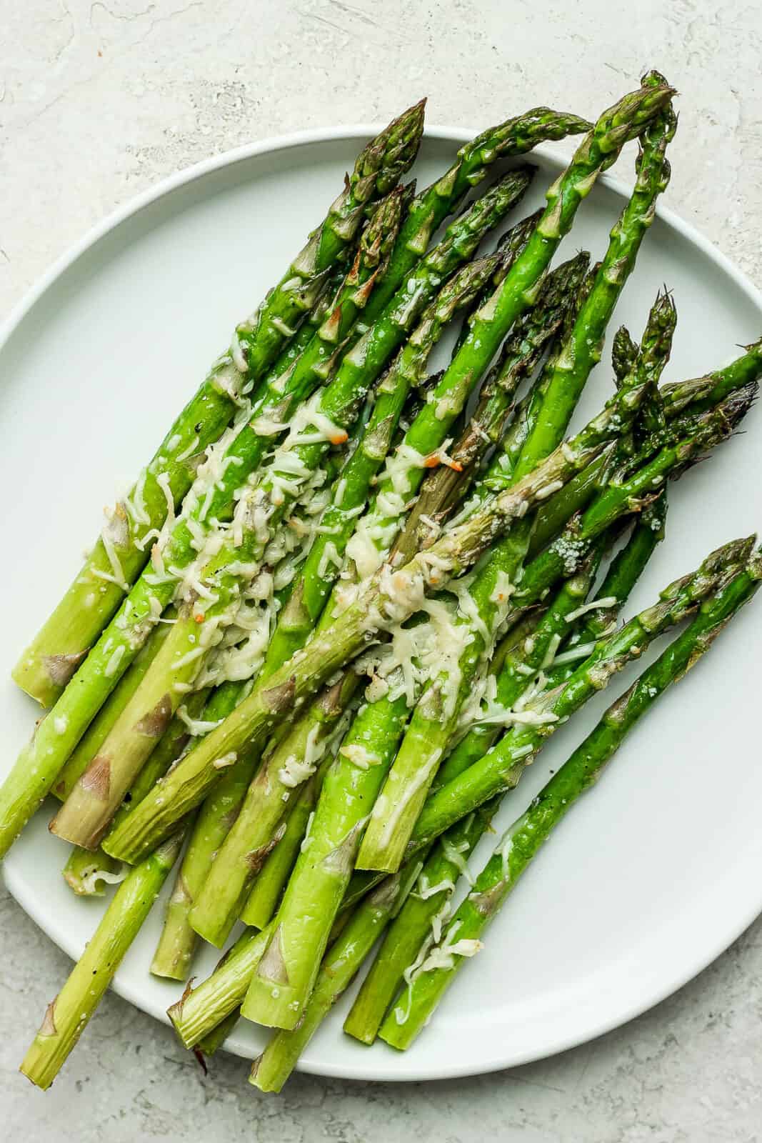 A bunch of air fryer asparagus on a white plate topped with parmesan.