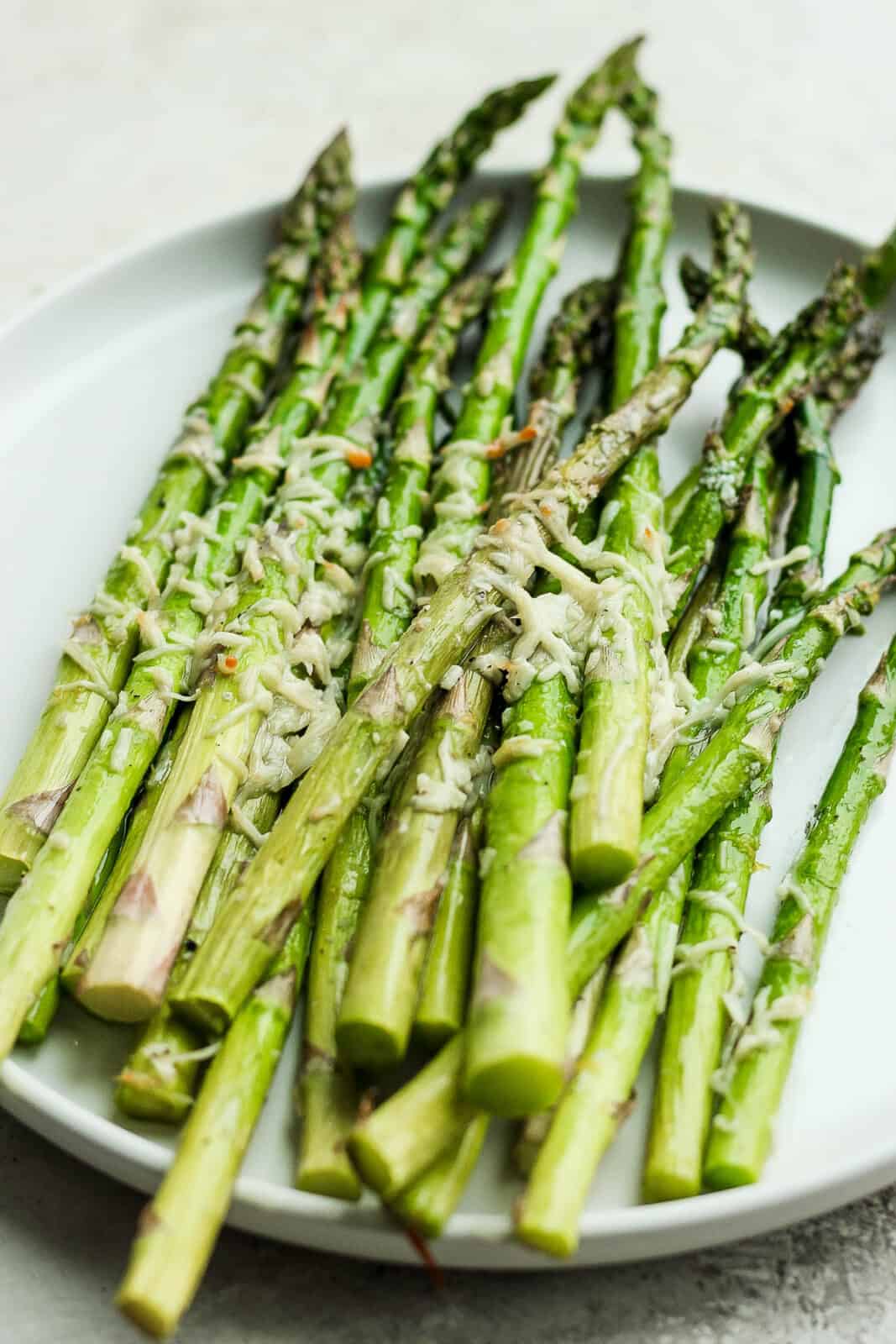 Air fryer asparagus topped with melted parmesan on a white plate.