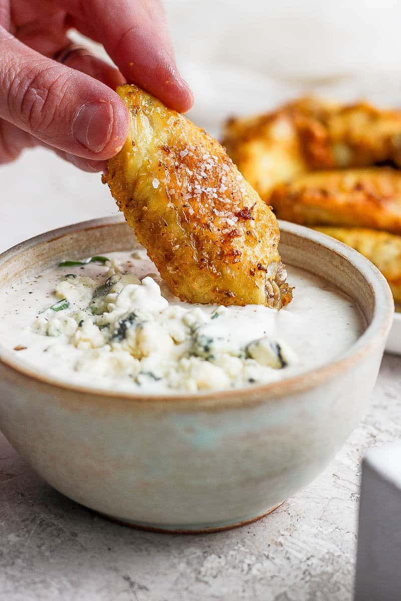 A chicken wing being dipped in blue cheese dressing.