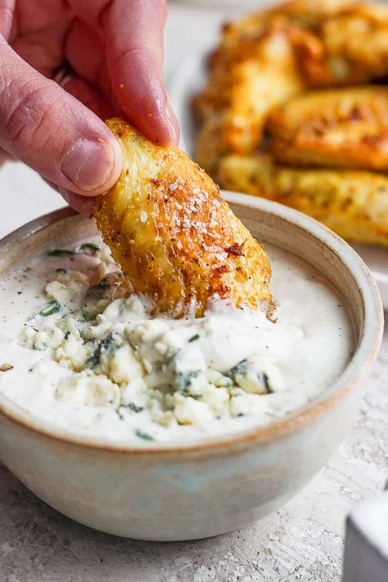 A crispy air fryer chicken wing being dipped in a bowl of blue cheese dressing.