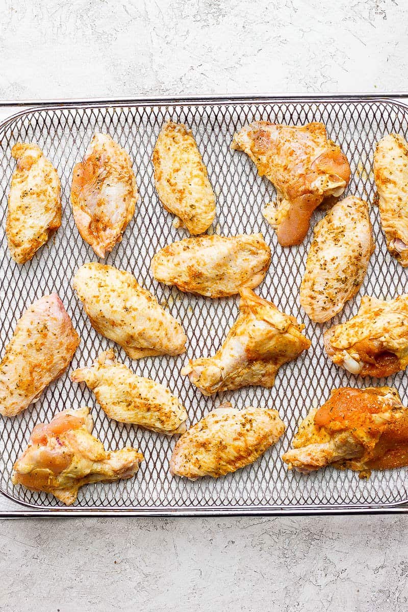 Chicken wings covered with dry rub and olive oil in an air fryer basket.