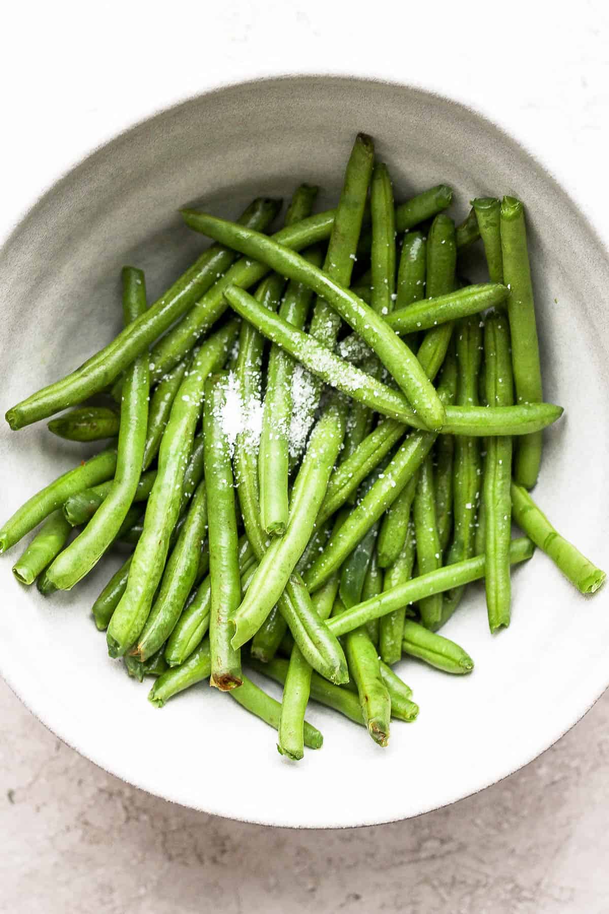 Plain green beans in a white bowl with  salt.