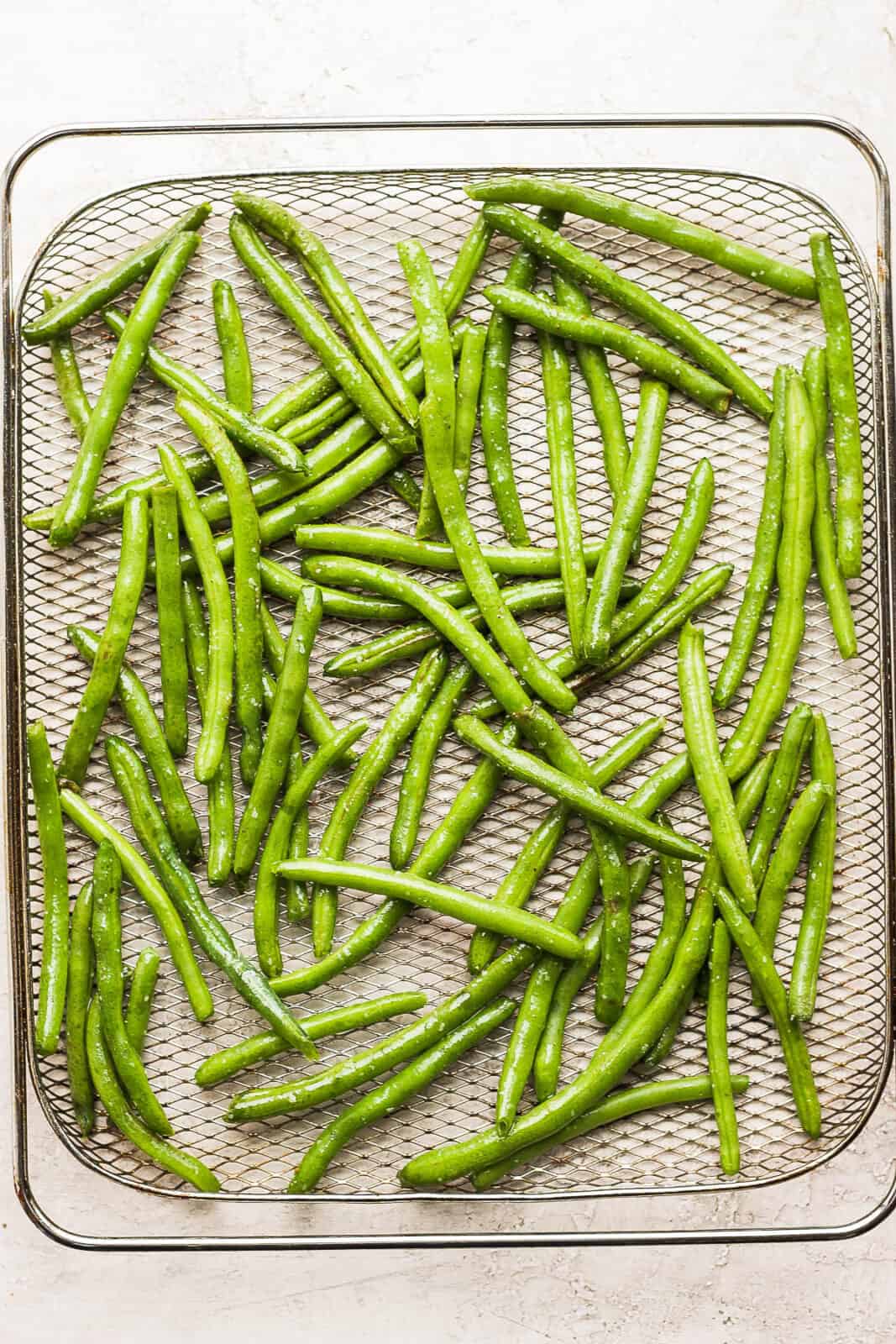 Seasoned green beans in an air fryer basket. 