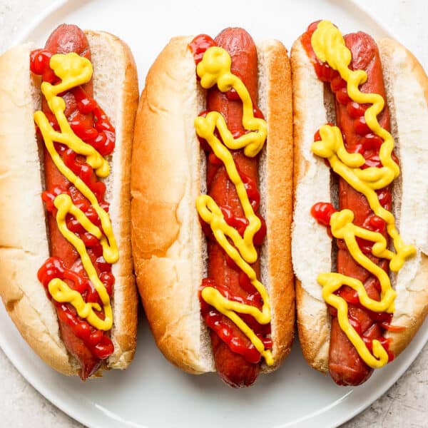 Plate of three hot dogs with ketchup and mustard that have been cooked in the air fryer.