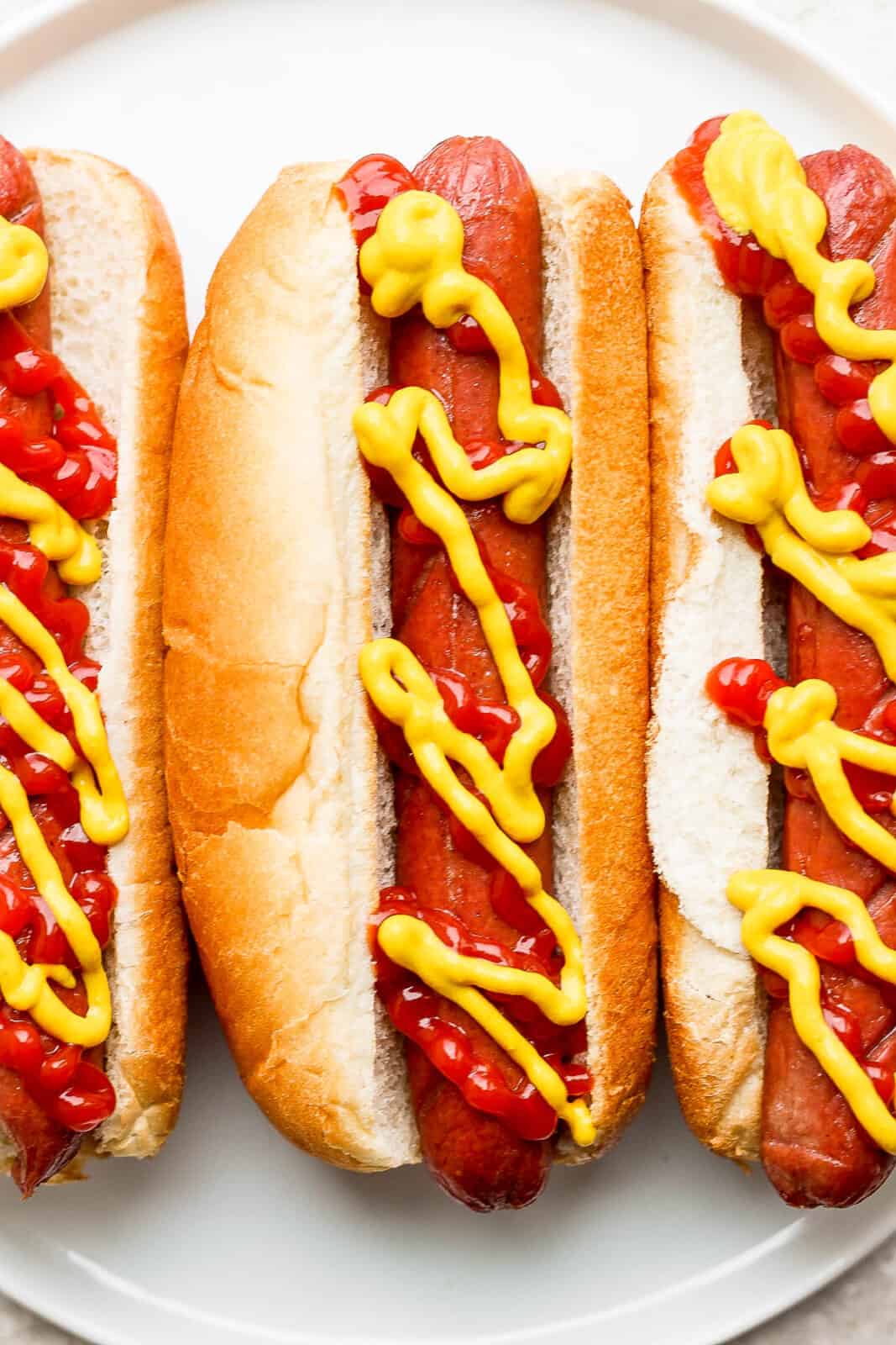 Three hot dogs in buns with condiments on top.