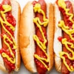 Plate of three hot dogs with ketchup and mustard that have been cooked in the air fryer.