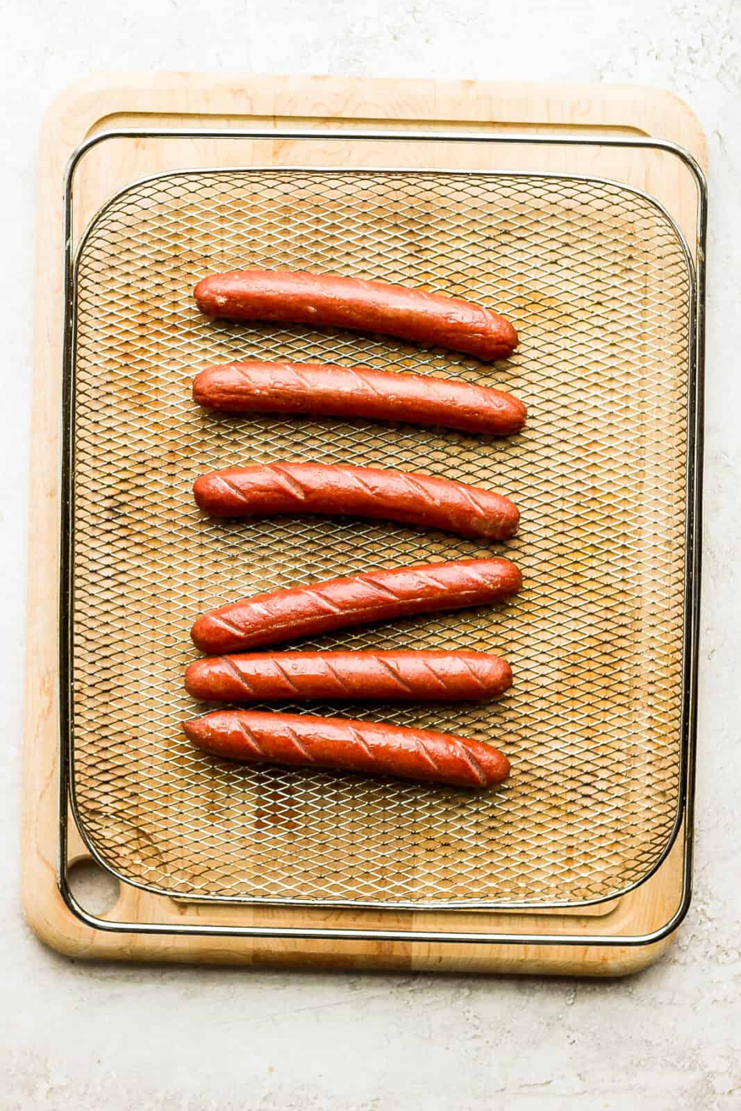Six air fried hot dogs in an air fryer basket.