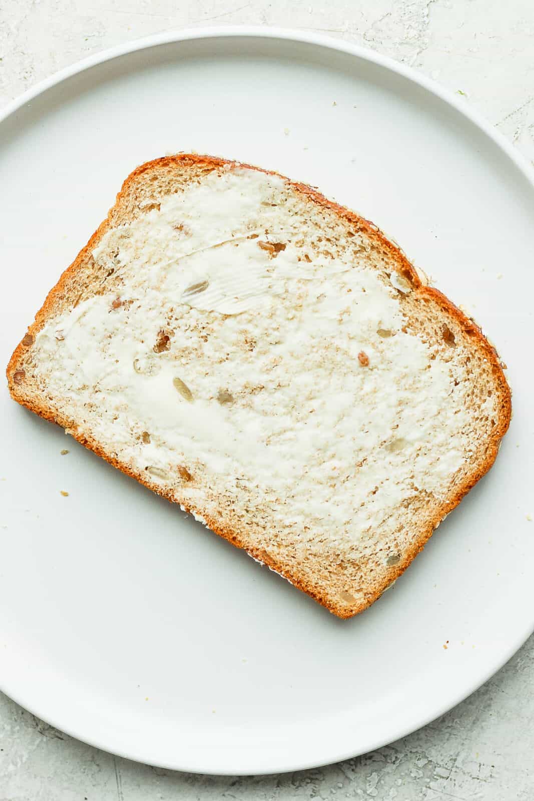 A slice of bread on a plate with butter spread on it.