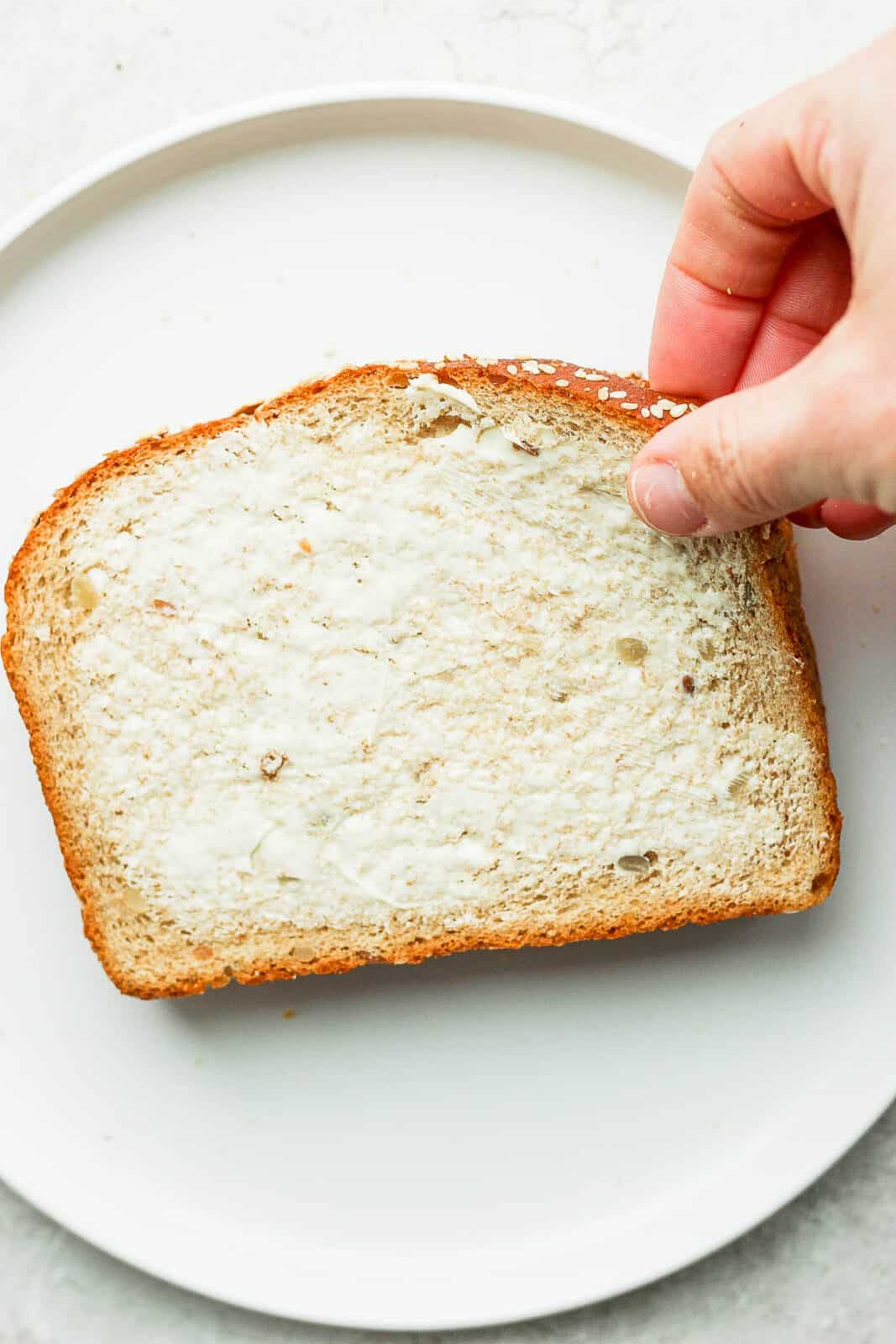 A hand placing the top piece of buttered bread on the sandwich.