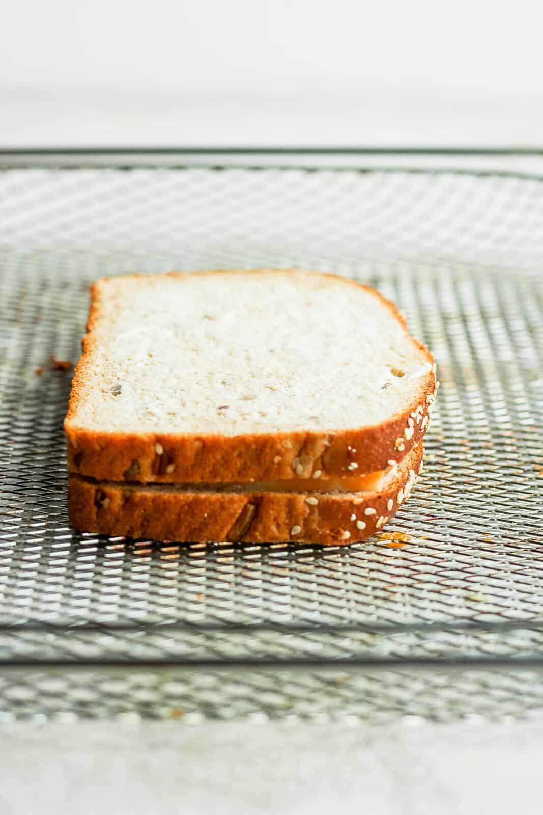 An air fryer grilled cheese sandwich on an air fryer basket before cooking.