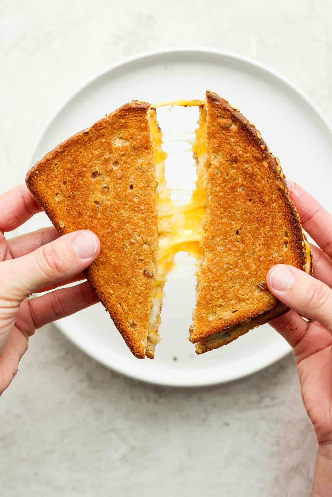 Two hand pulling apart an air fryer grilled cheese to show the cheesy goodness.