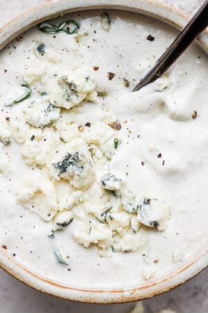 A small bowl of homemade blue cheese dressing with the a spoon sticking out.