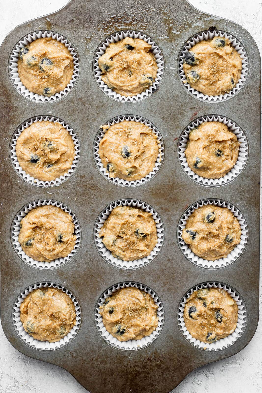 The blueberry banana muffin batter added to muffin cups in a muffin pan.