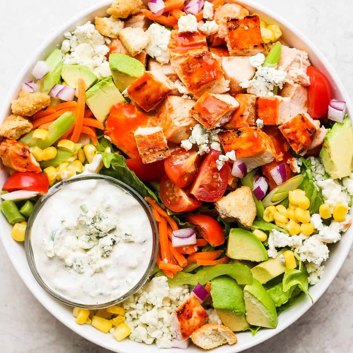 Big bowl of buffalo chicken salad with a cup of blue cheese dressing.