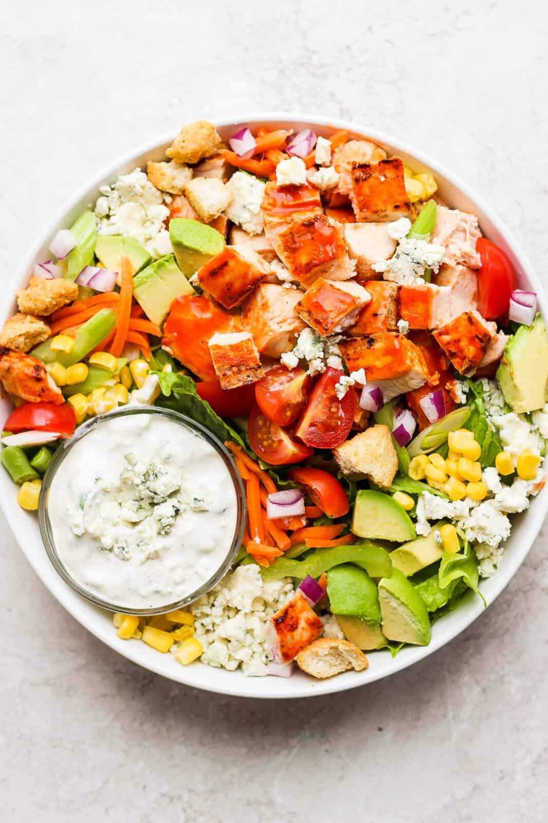 An ultimate buffalo chicken salad with a small dish of blue cheese dressing.