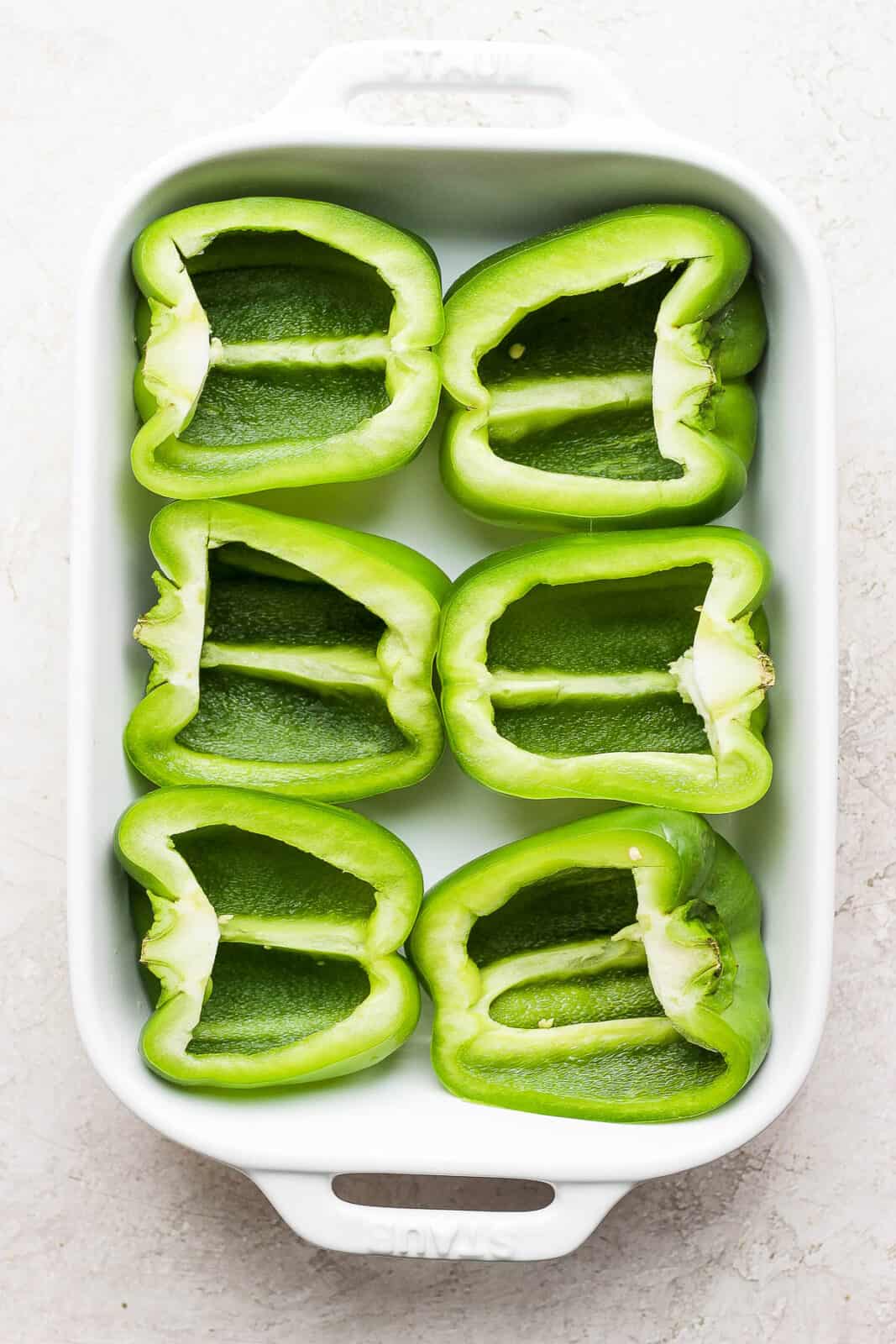 Green bell pepper halves in a baking dish.