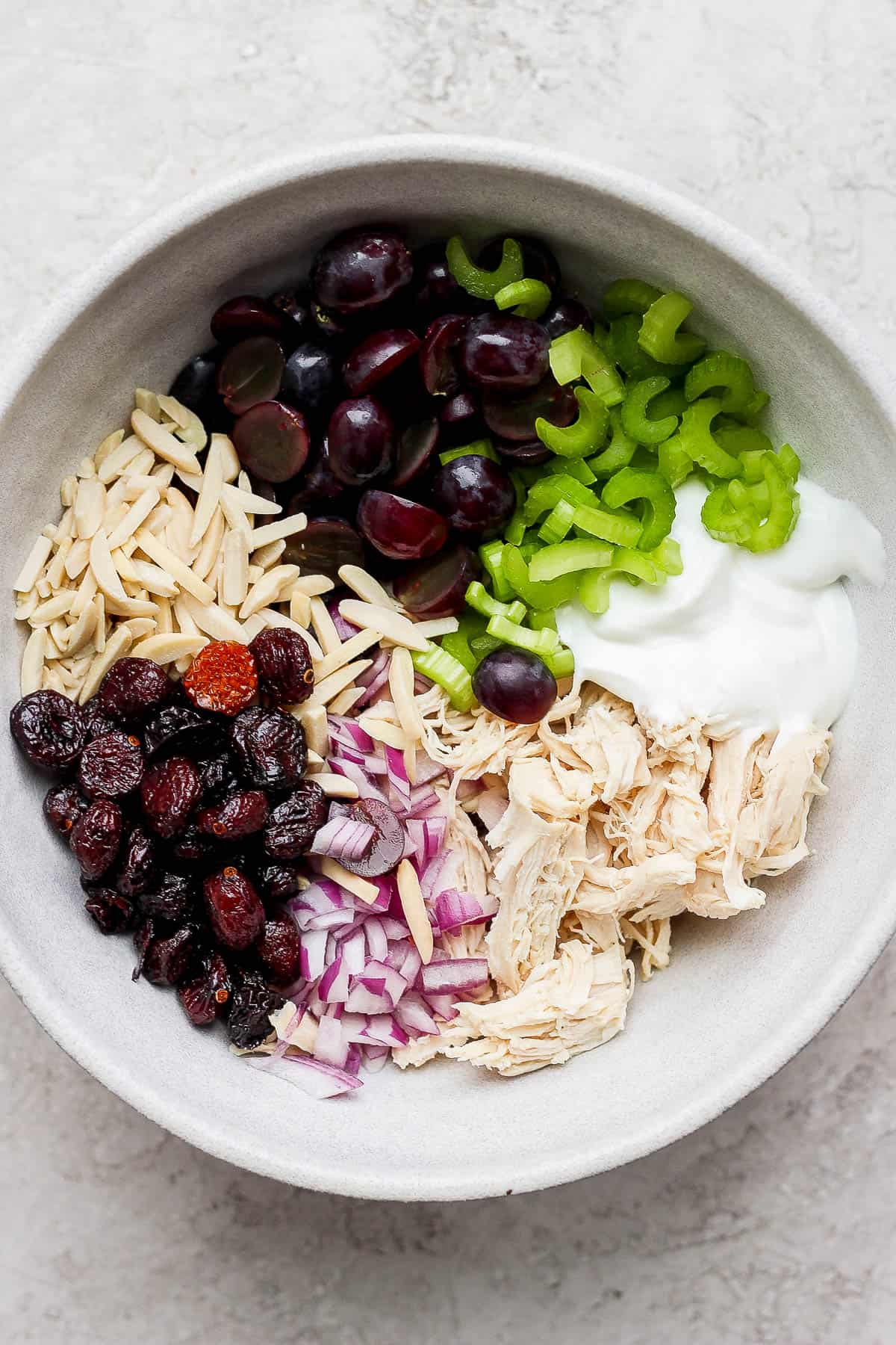 Sliced grapes, chopped celery, greek yogurt, shredded chicken, chopped onions, and slivered almonds in a white bowl.