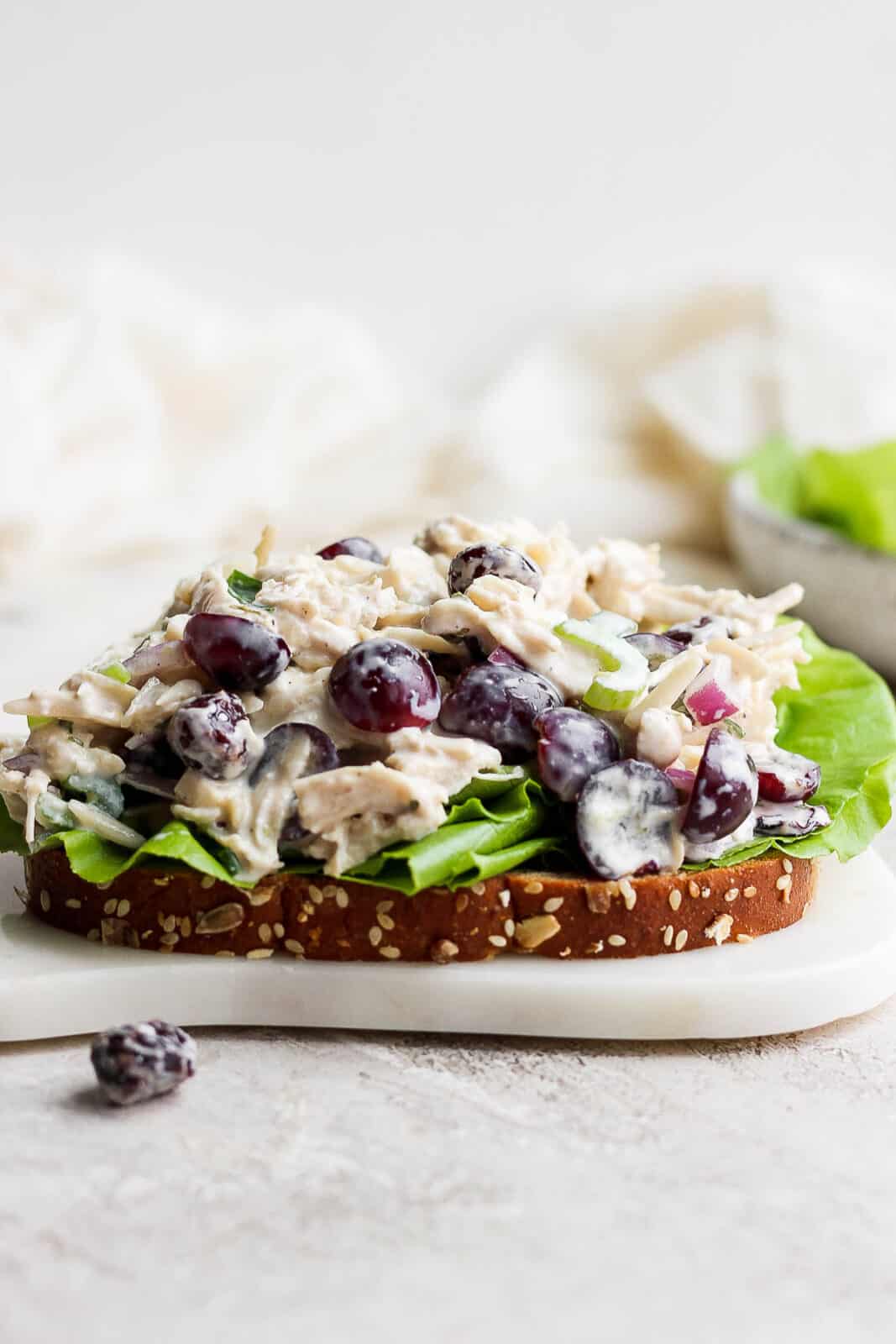Greek yogurt chicken salad topped on a slice of bread with butter lettuce sitting on a white cutting board.
