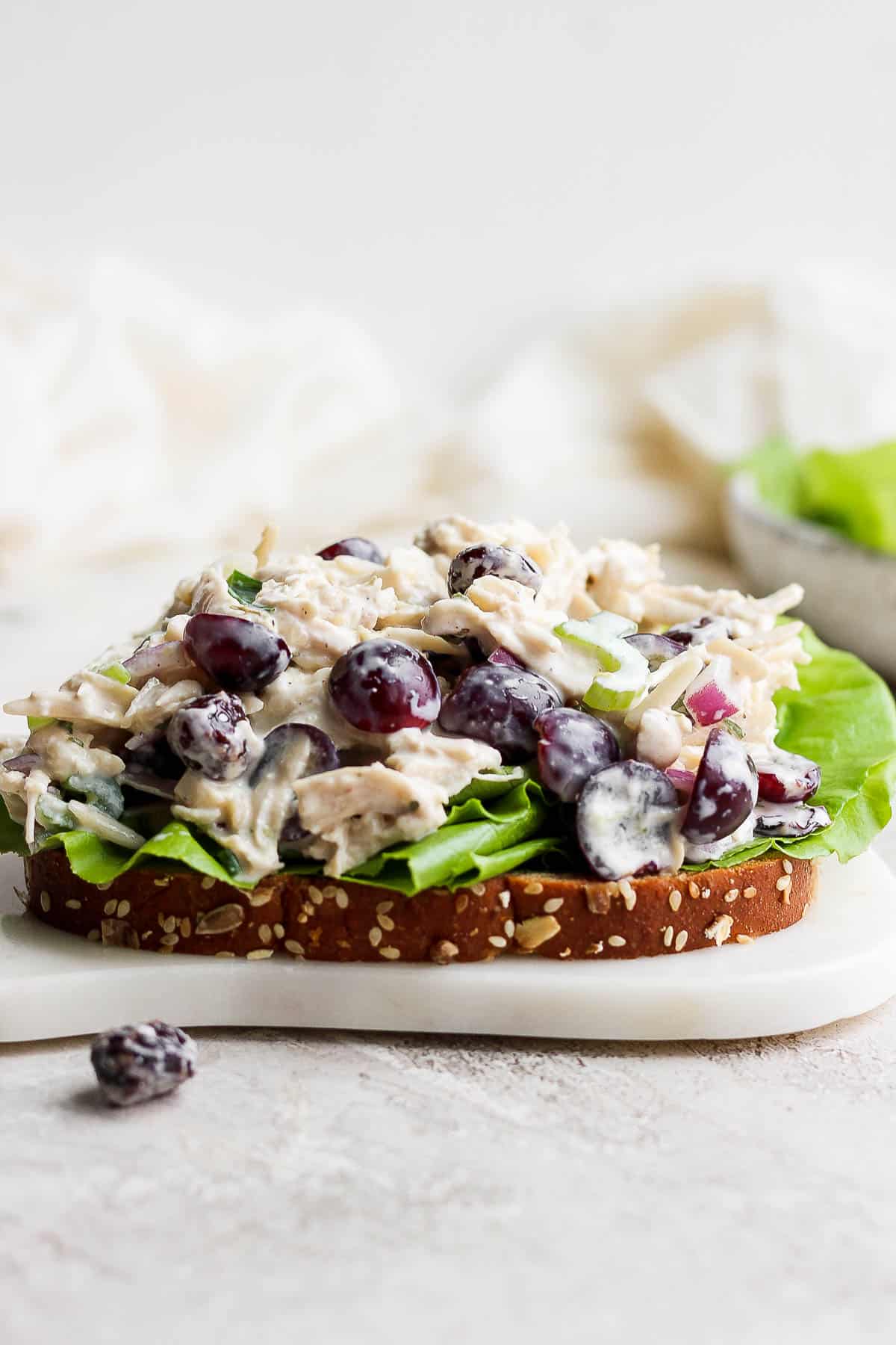 Greek yogurt chicken salad topped on a slice of bread with butter lettuce sitting on a white cutting board.