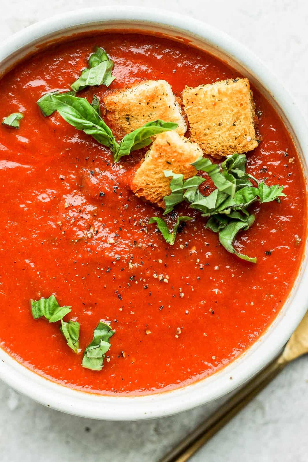 Creamy tomato basil soup in a bowl with homemade croutons and fresh basil on top.