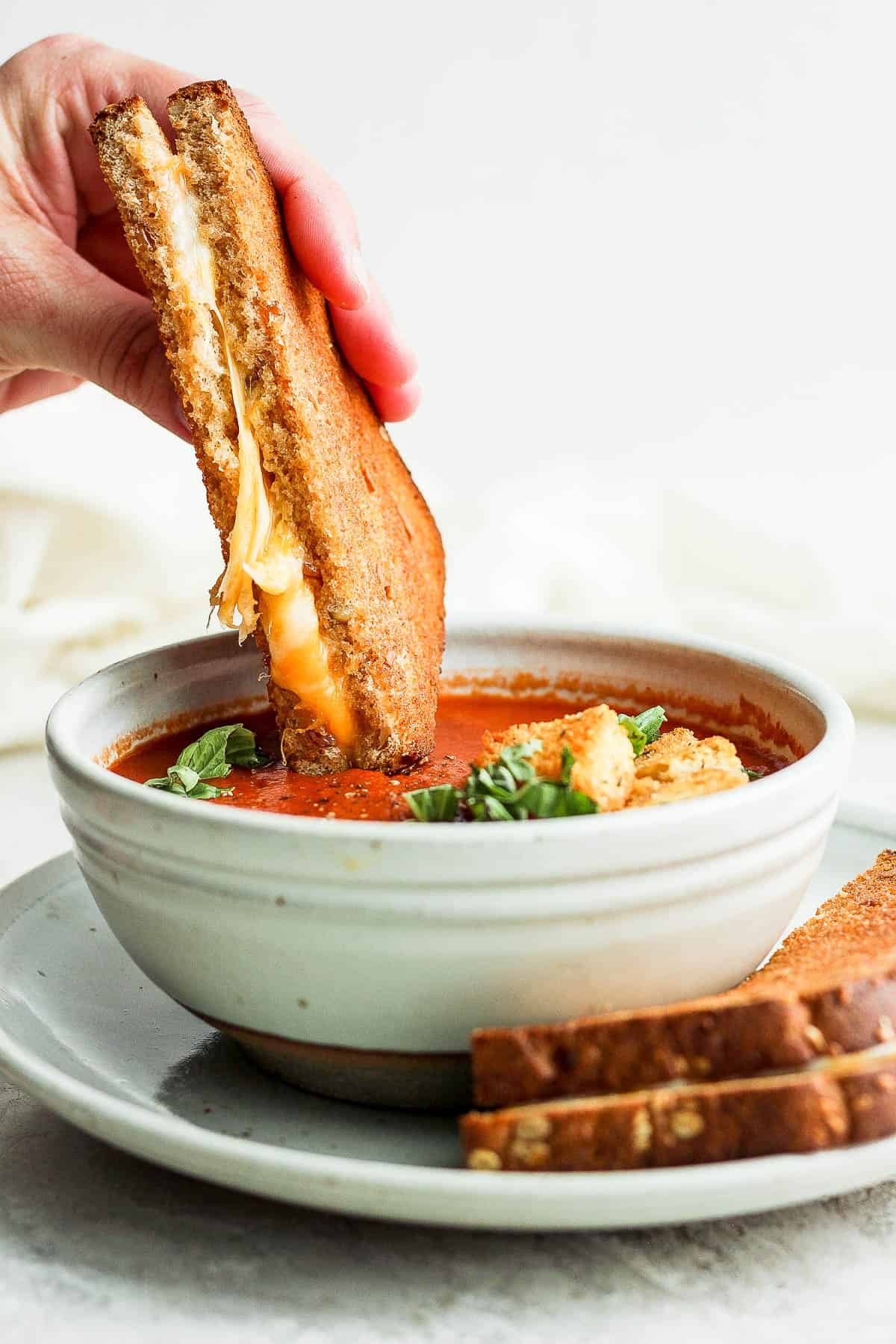 A grilled cheese being dipped in a bowl of tomato soup.