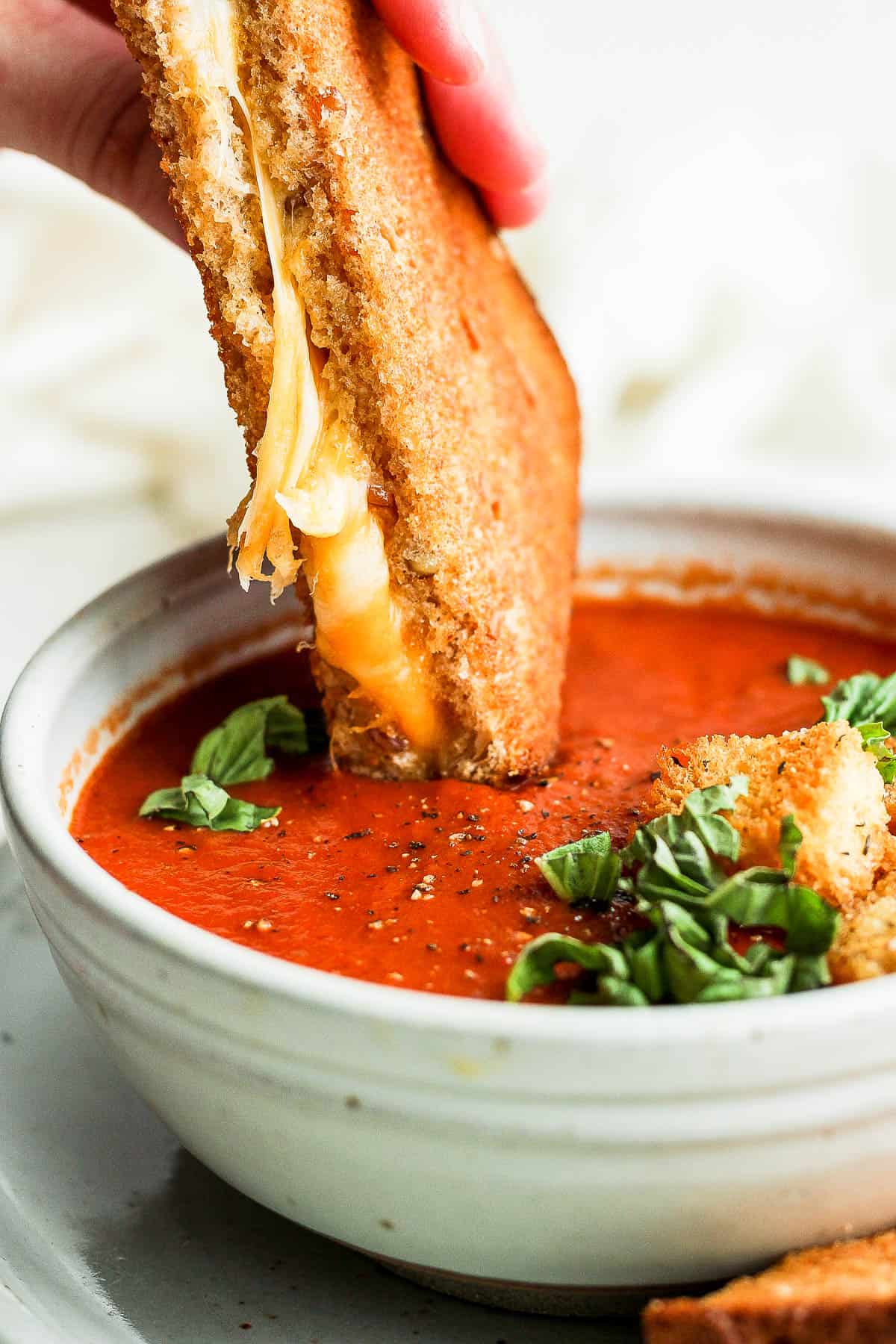 Homemade tomato soup with canned tomatoes in a bowl with a hand dipping in a grilled cheese into the soup.