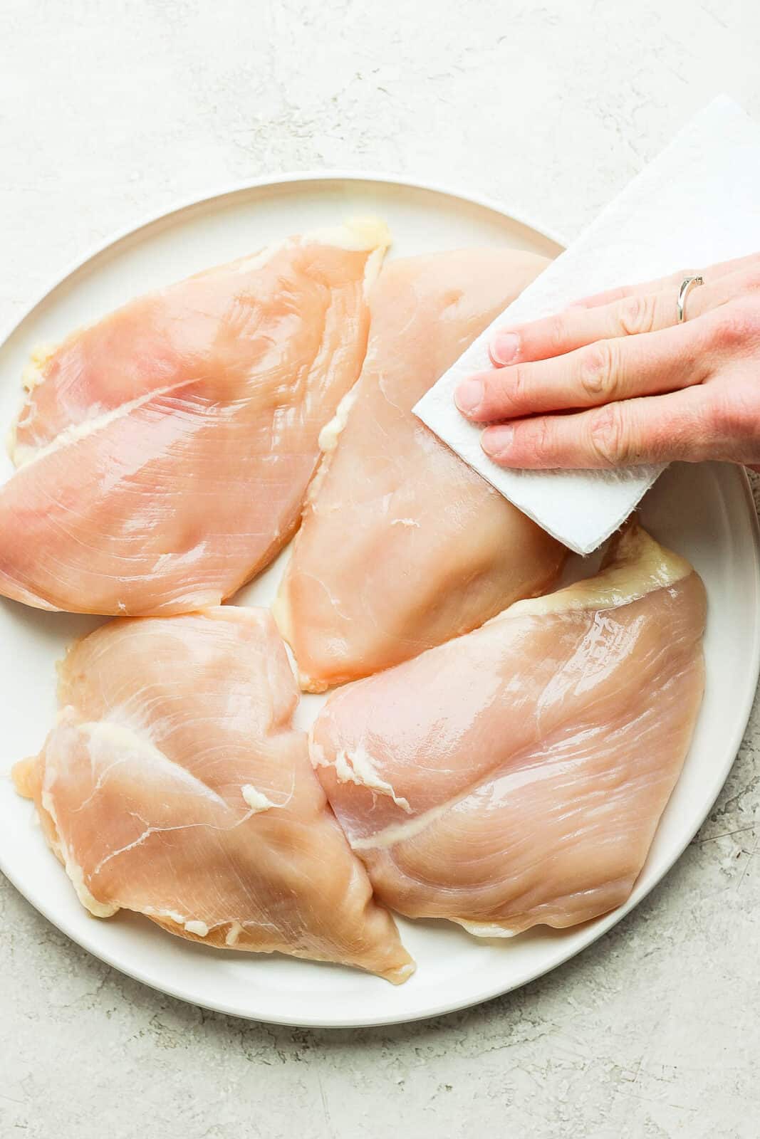 Raw chicken breasts being pat dry on a plate.