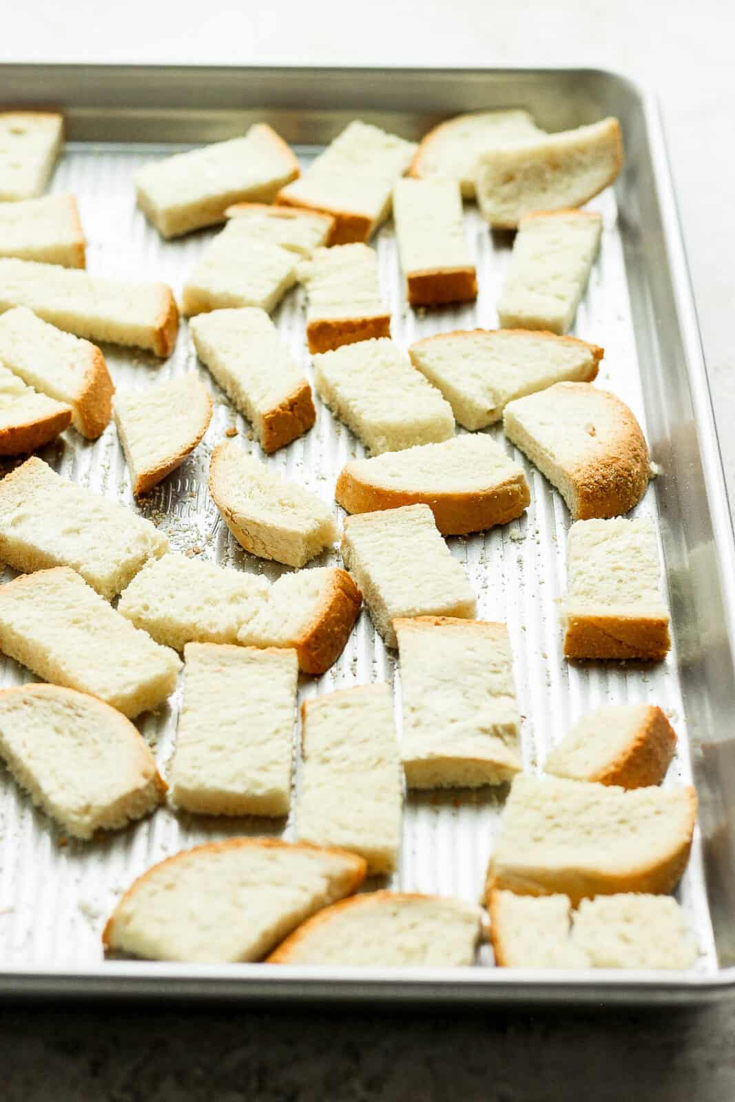 Cubed bread spread out on a baking sheet.