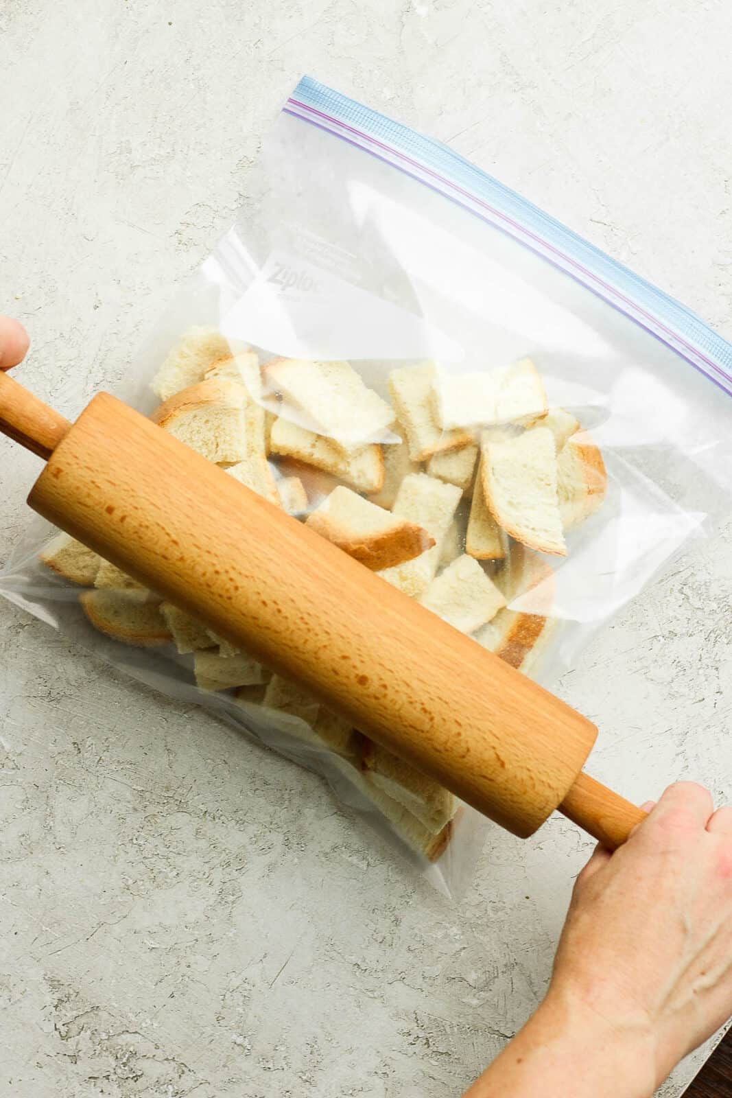 Cubed bread in a sealed ziplock bag with a rolling pin over the top. 
