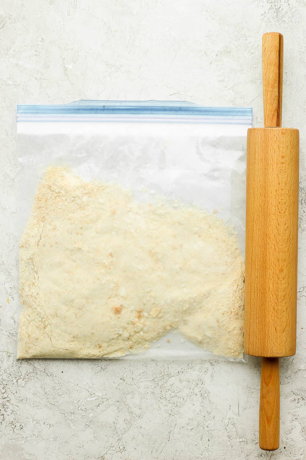 Breadcrumbs in a sealed ziplock bag with a rolling pin next to it. 