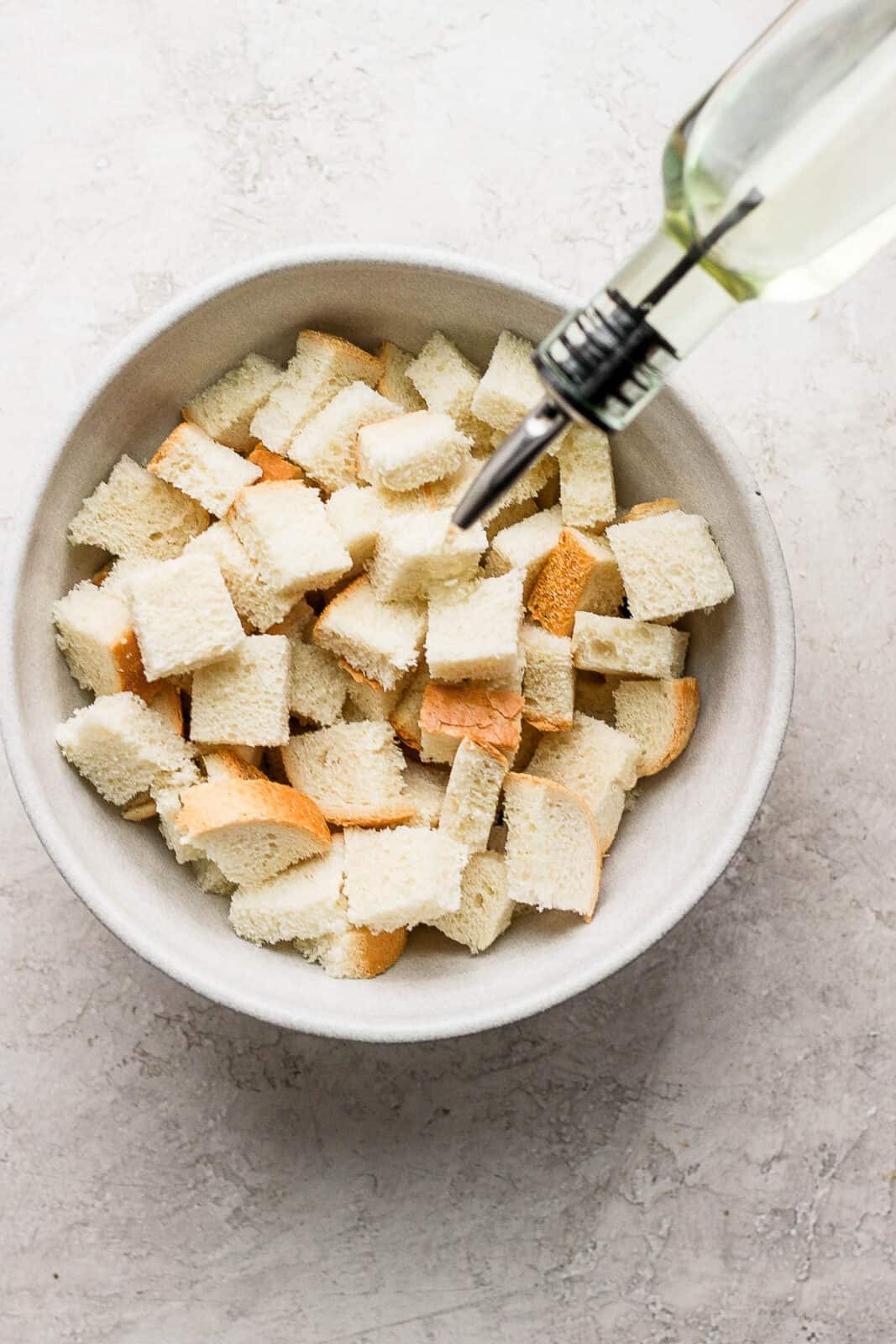 Cubed bread in a bowl with olive oil being drizzled on top.