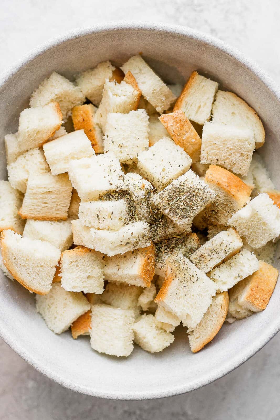 Cubed bread in a bowl with seasonings added on top.