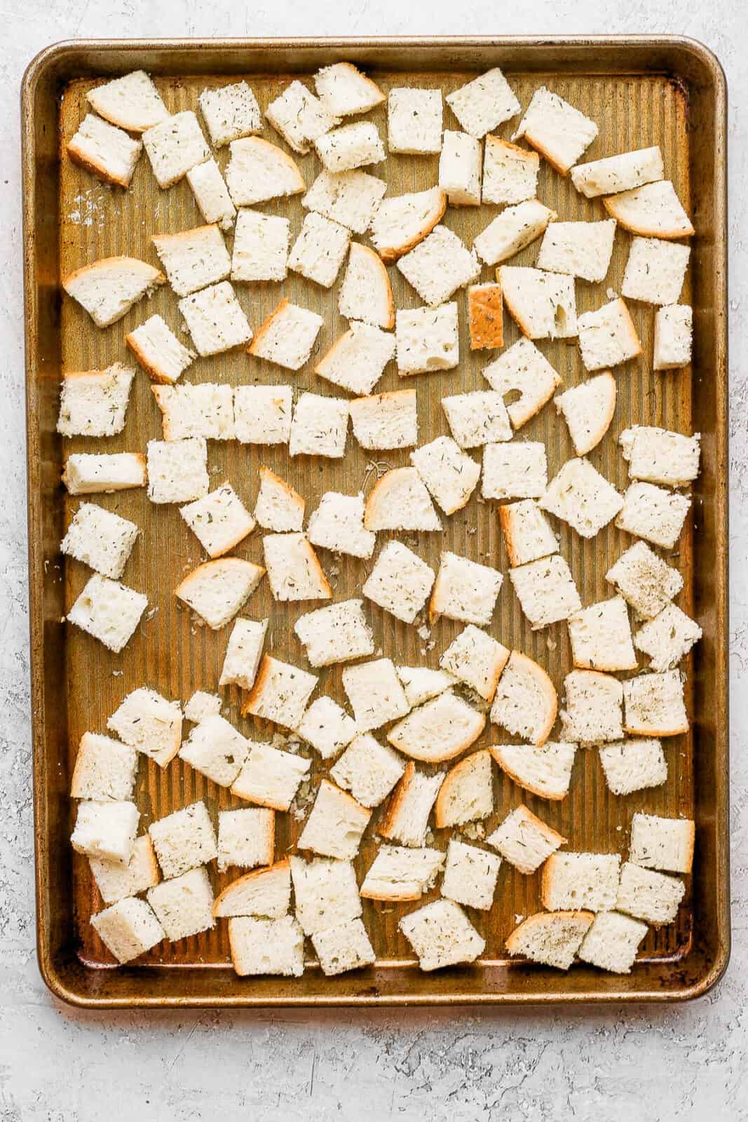 Seasoned bread pieces on a baking sheet before baking.