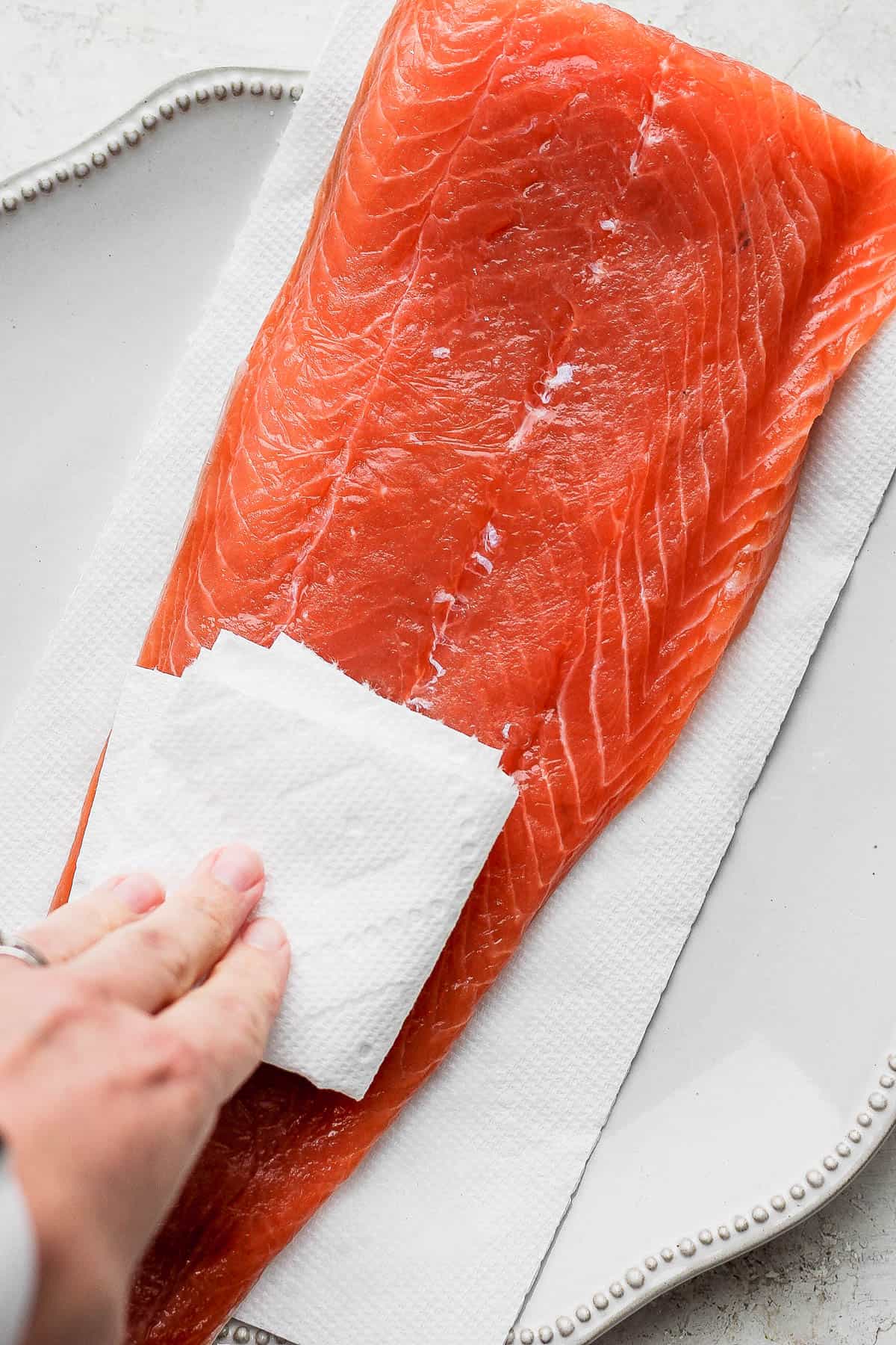 Cured salmon on a plate and someone is patting it dry.