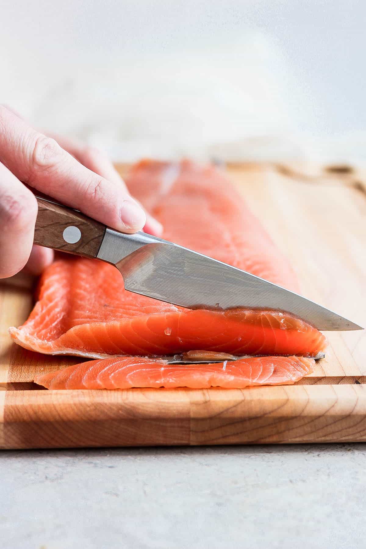 Someone thinly slicing the cured salmon.