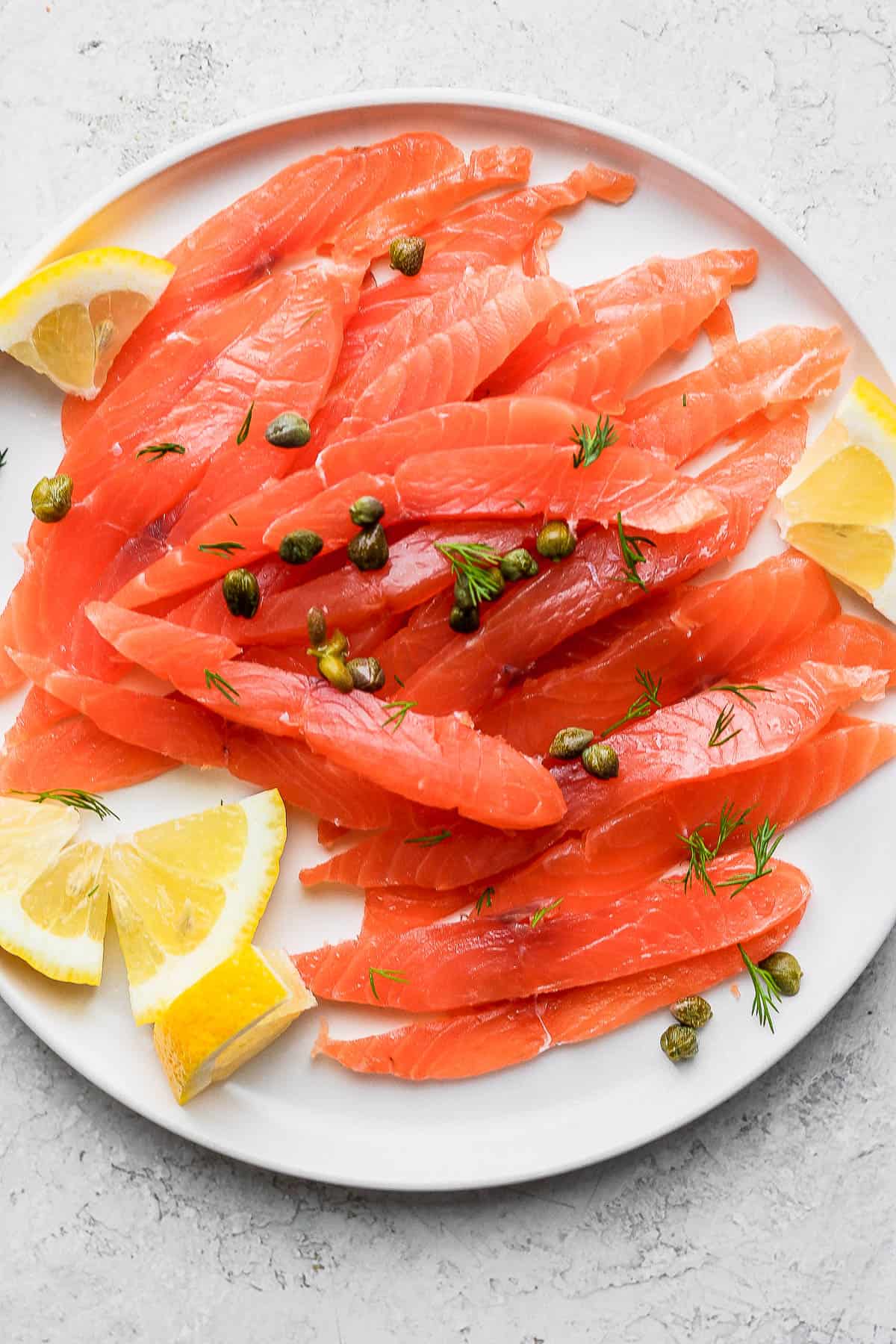 Cured salmon on a plate with lemon wedges, dill and capers.