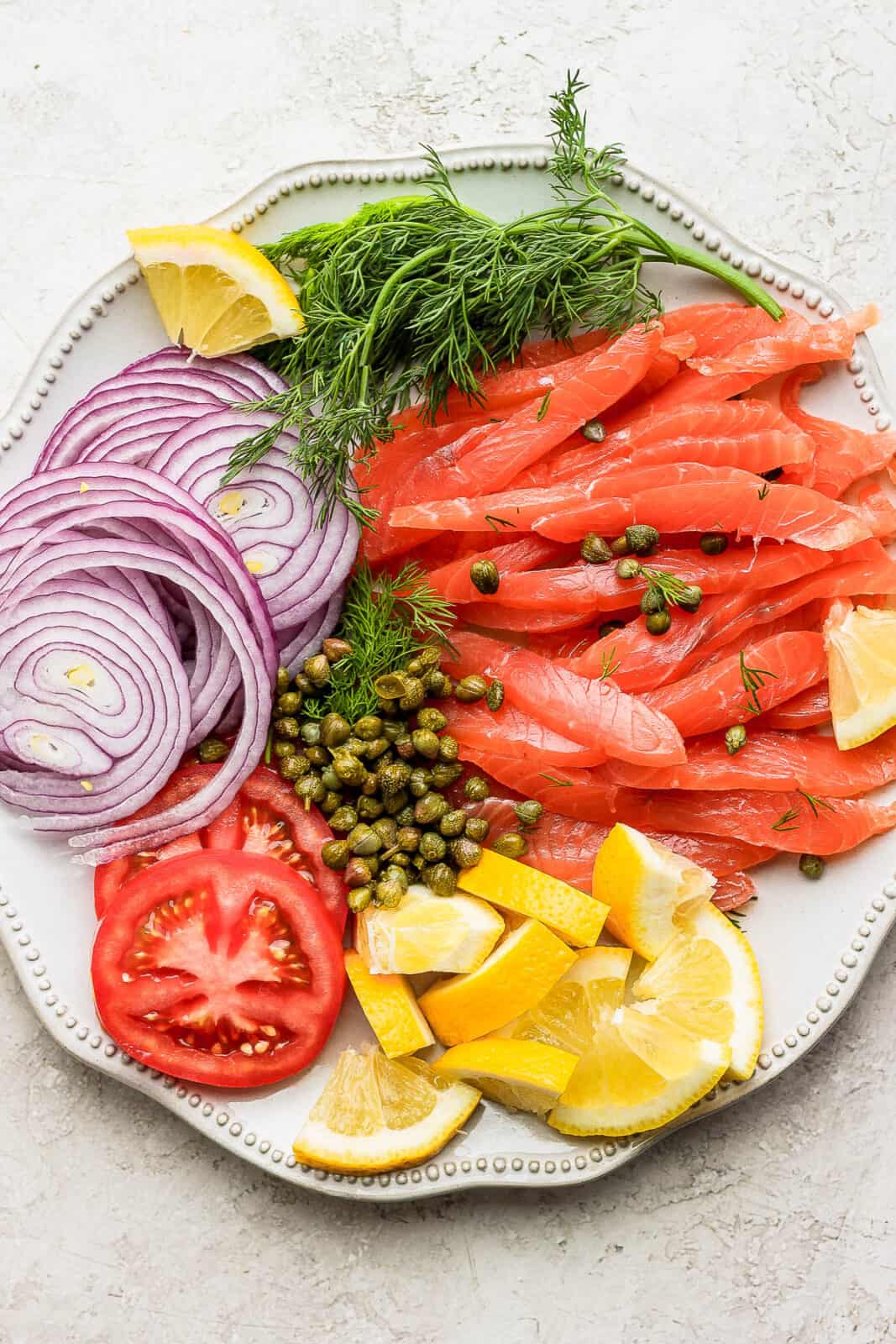 A platter of homemade salmon, capers, red onions, fresh dill, tomato and lemon. 