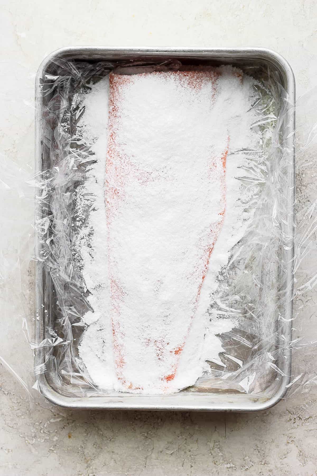 Kosher salt covering a raw salmon fillet in a baking dish. 