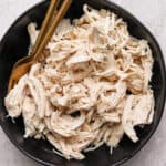 A bowl of poached chicken that has been shredded with two forks.