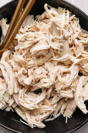 A bowl of poached chicken that has been shredded with two forks.